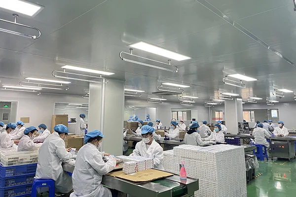 Workers in protective uniforms and blue caps assembling products on a production line in a clean, well-lit factory.